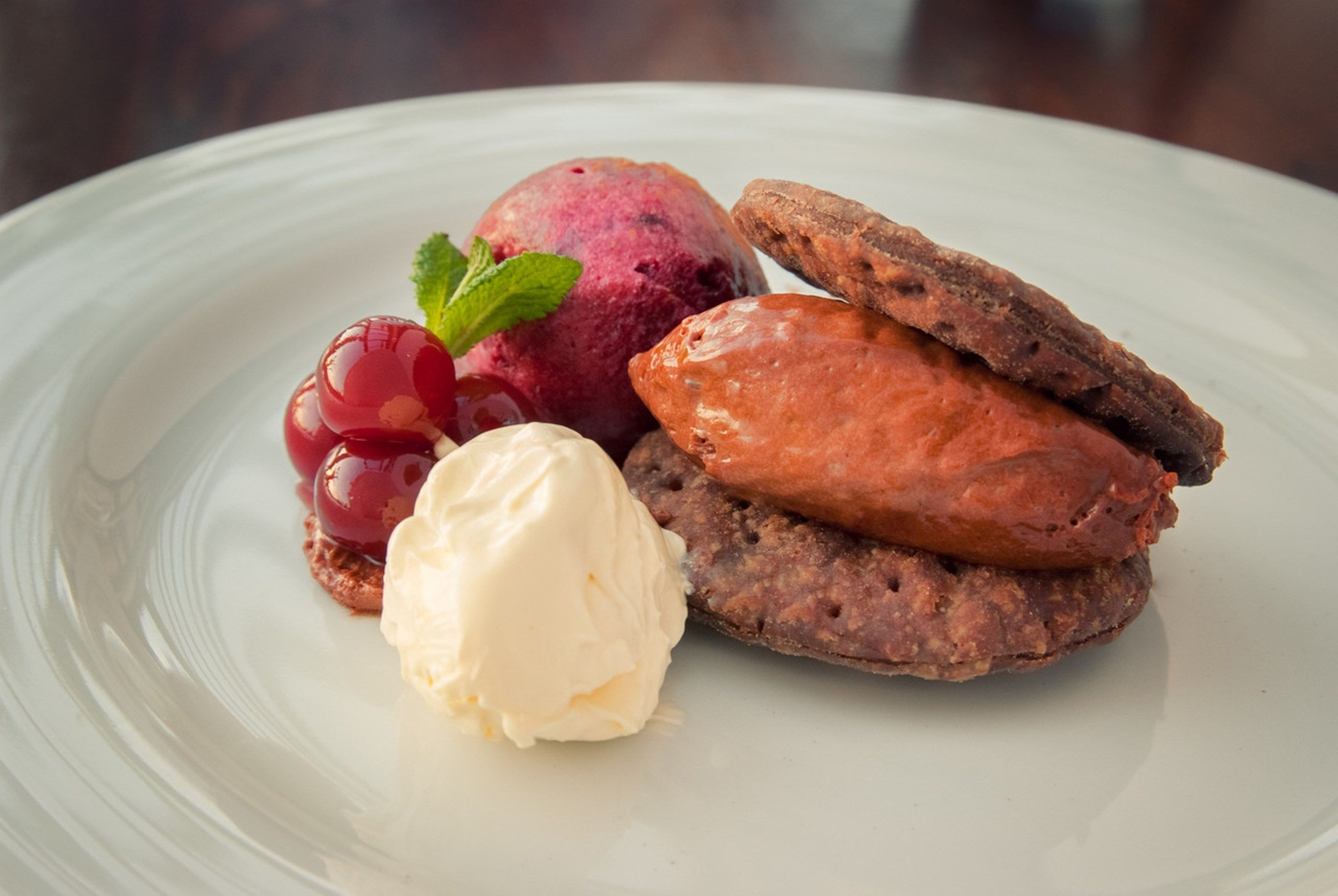 A dessert plate with a scoop of vanilla ice cream, a scoop of berry compote, a slice of cake, and a piece of fruit.