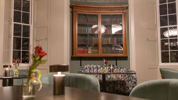 A room with a large wooden bookcase, a table with a vase of flowers, and a patterned sofa.