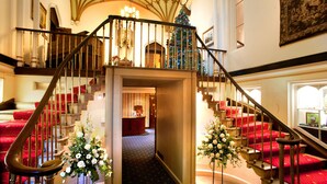 A grand staircase with red carpeted steps and a chandelier, leading to a second-floor area with a Christmas tree. - Dalhousie Castle (Bonnyrigg)