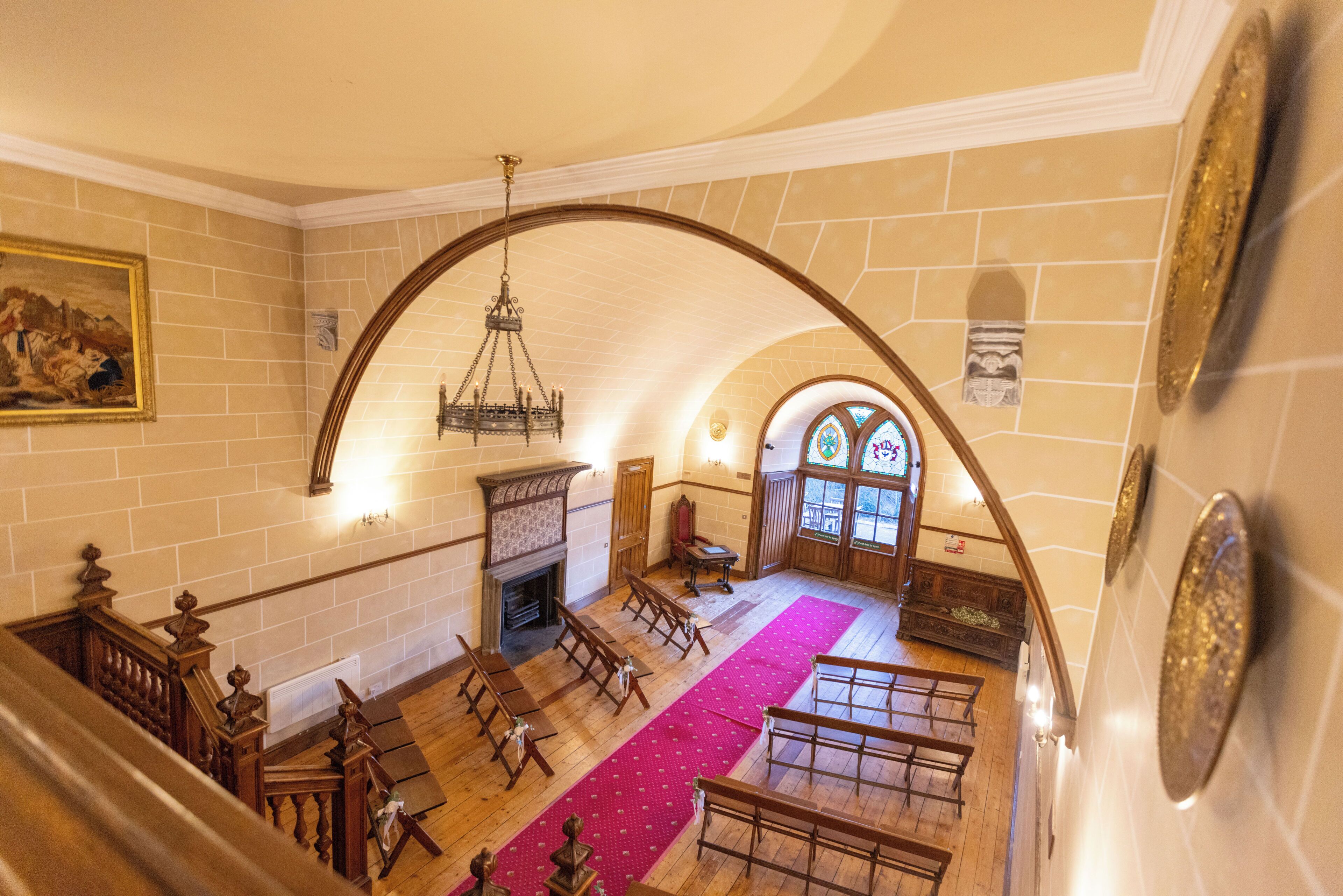 Interior de iglesia con bancales, una escalera de madera, un candelabro y un vitral.