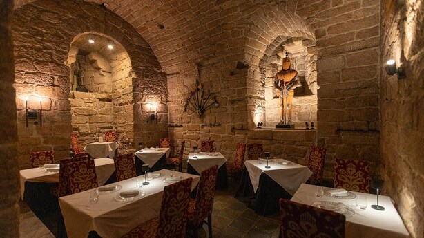 A stone-walled dining area with tables set for four, each with a white tablecloth and patterned chairs.