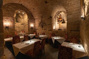 Comedor de paredes de piedra con mesas preparadas para cuatro comensales, cada una con mantel blanco y sillas estampadas.
