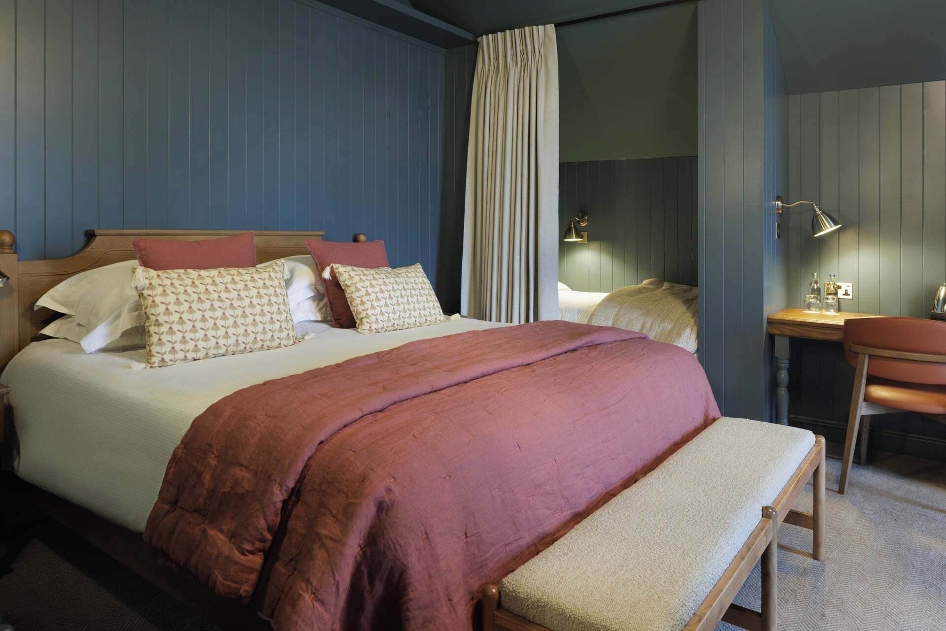 A hotel room with a large bed, a desk, and a bench.