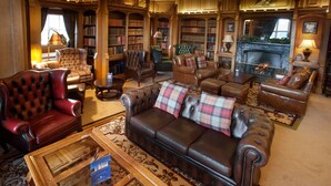 A library with leather sofas, bookshelves, and a fireplace.
