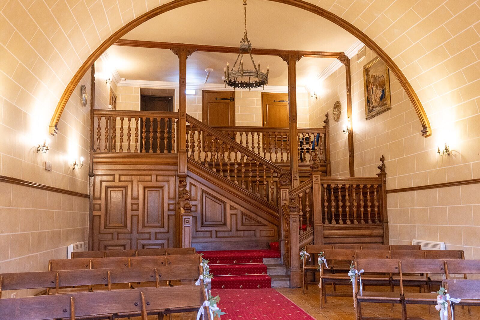 Interior de una iglesia con bancos de madera, un pasillo cubierto de alfombra roja y una escalera de madera con barandilla.