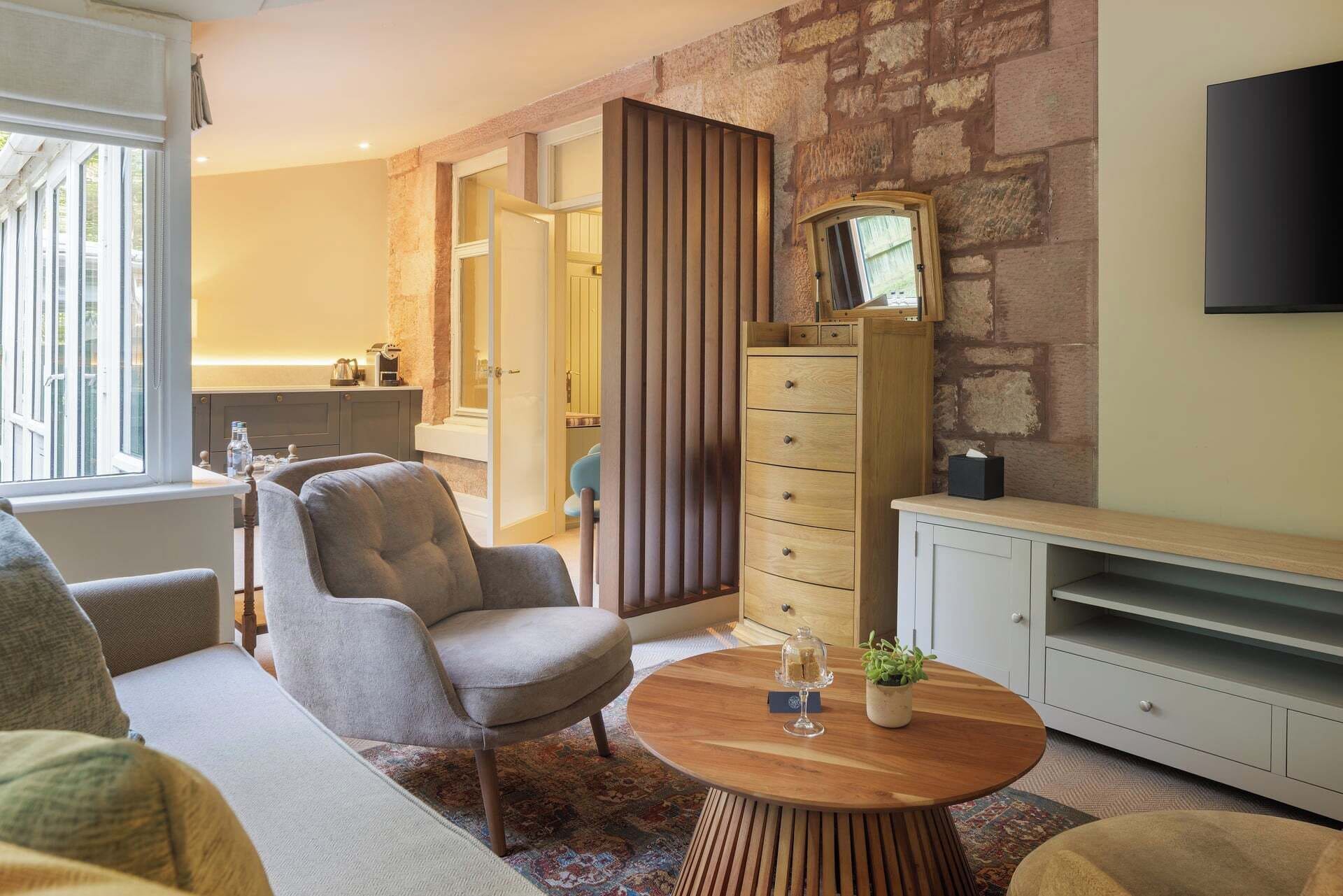 A living room with a sofa, armchair, coffee table, and a TV on a stand.