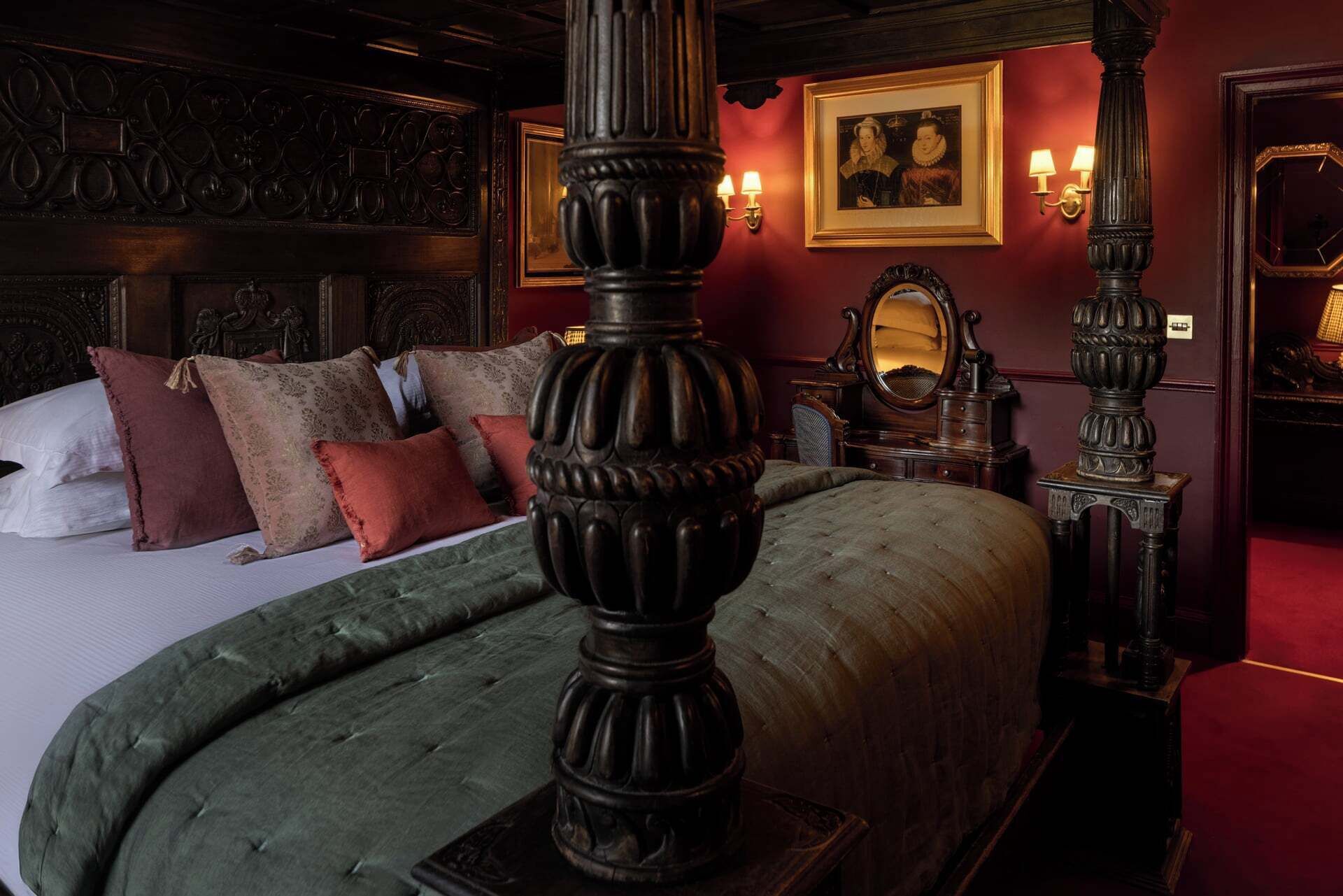 Una habitación con una cama grande, muebles ornamentales y una pared roja con obras de arte enmarcadas.