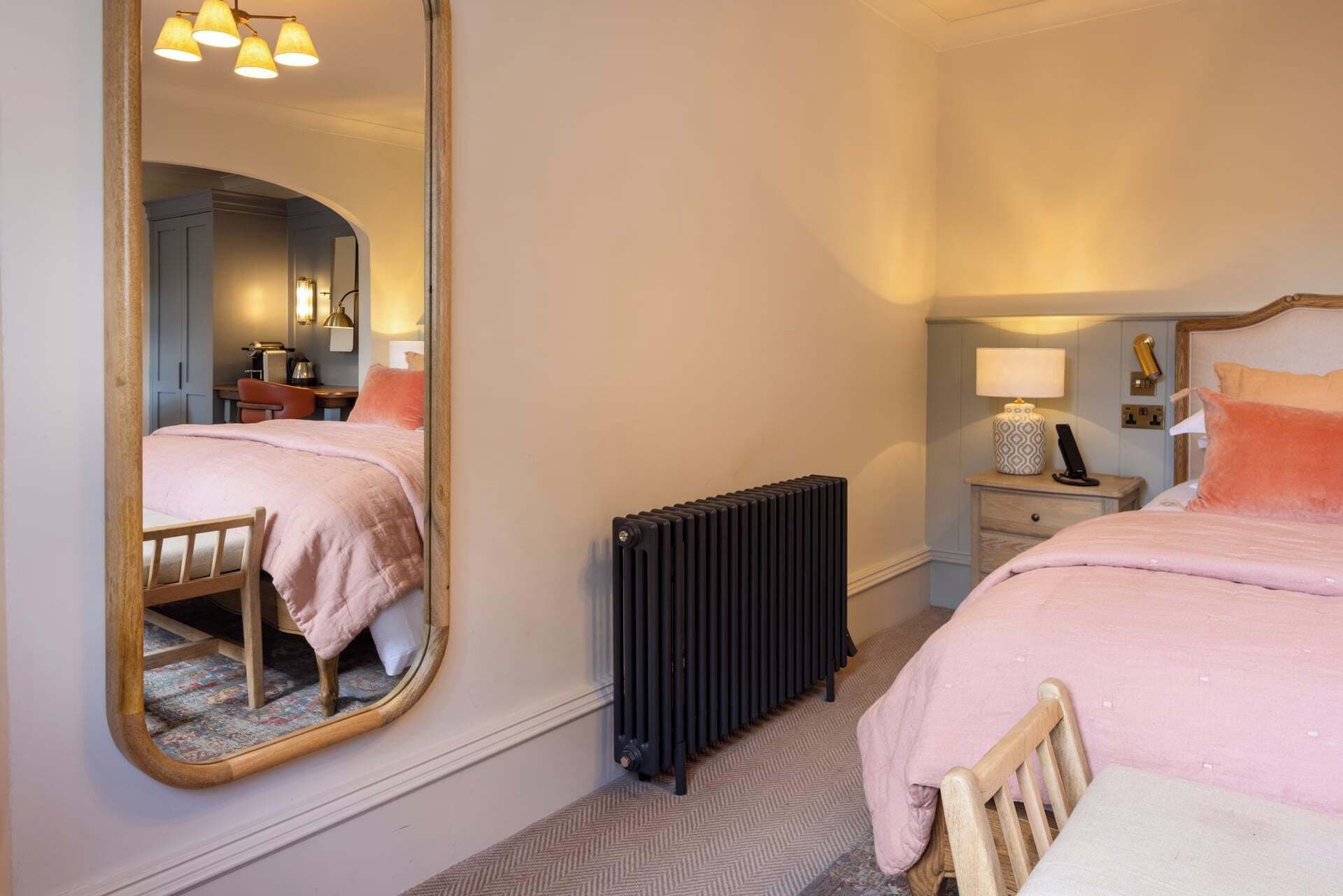 A bedroom with a large mirror, a radiator, a bedside table with a lamp, and a chair.