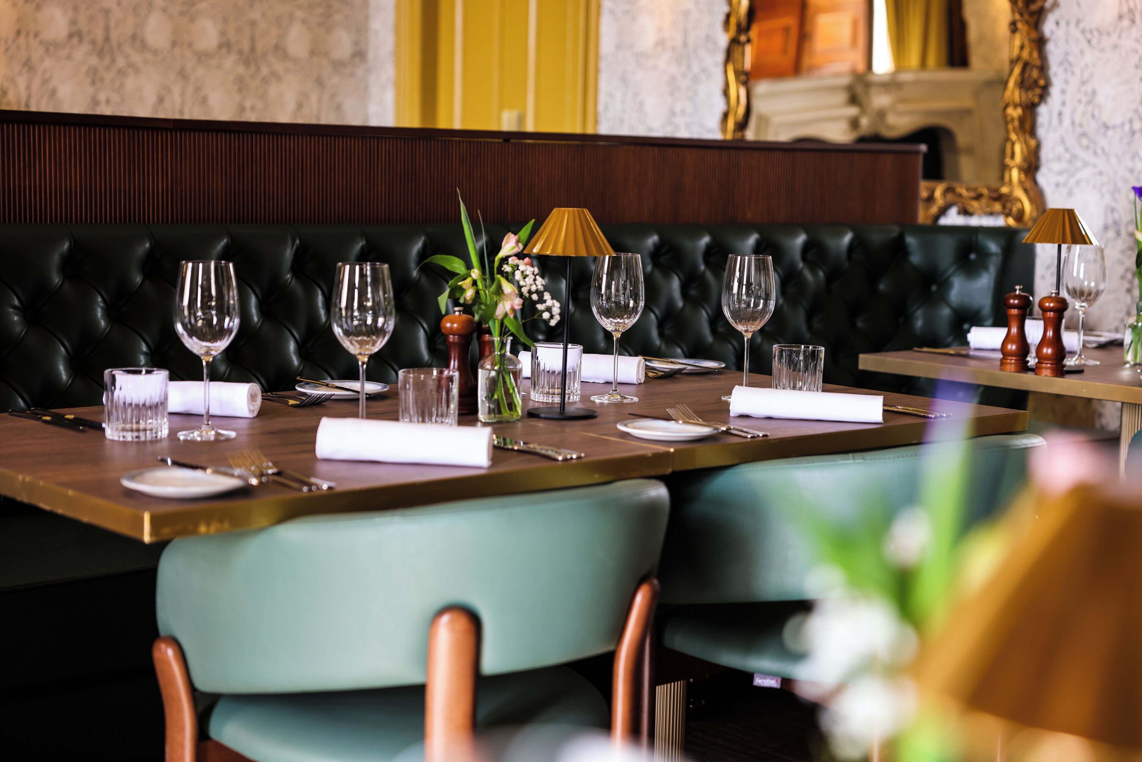 Un comedor con una mesa larga dispuesta para una comida, un asiento tipo banqueta de cuero negro al fondo y un jarrón con flores sobre la mesa.