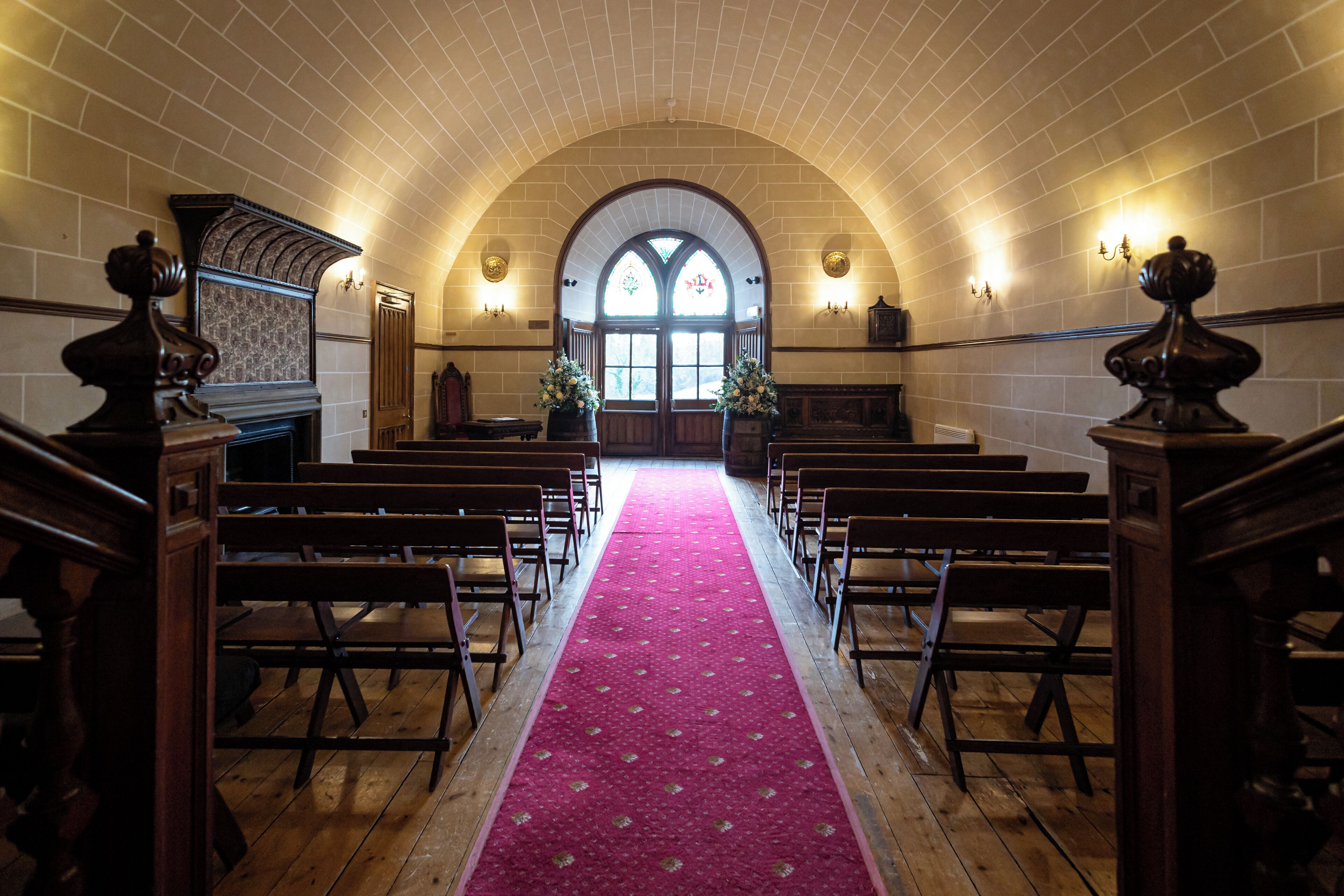 Interior de iglesia de estilo arqueado con bancas, alfombra roja y vidriera.