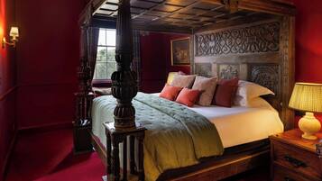 A four-poster bed with a green bedspread and multiple pillows, a wooden nightstand with a lamp, and a red carpeted floor.