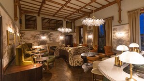 A room with a high ceiling, ornate wooden beams, a fireplace, and a bar area with stools and a round table.