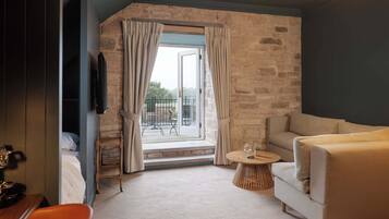 A hotel room with a stone wall, a sofa, a small round table with a glass, and a view of the outdoors.