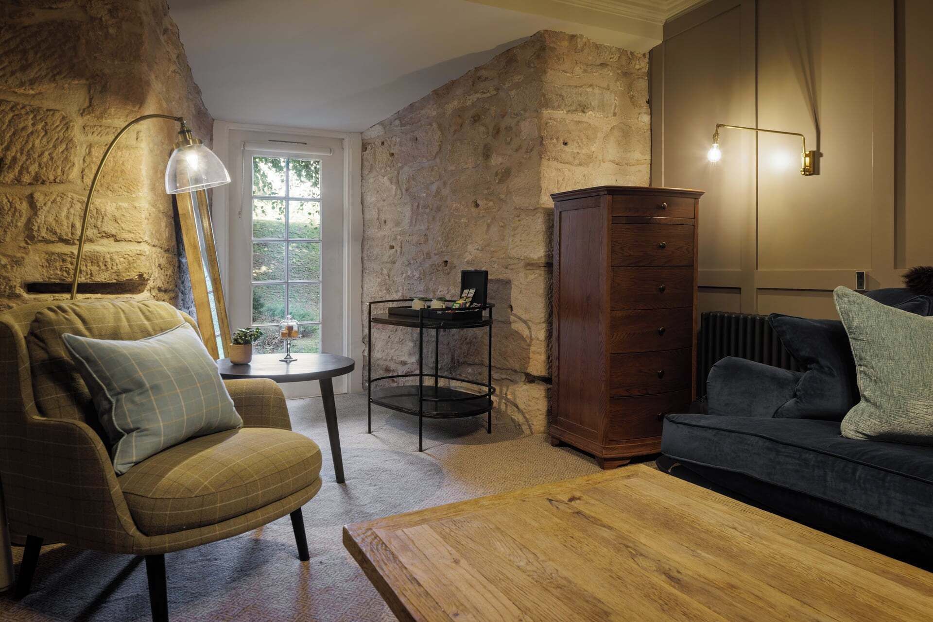 A cozy living room with a stone wall, a wooden cabinet, a dark sofa, a wooden coffee table, and a lamp.
