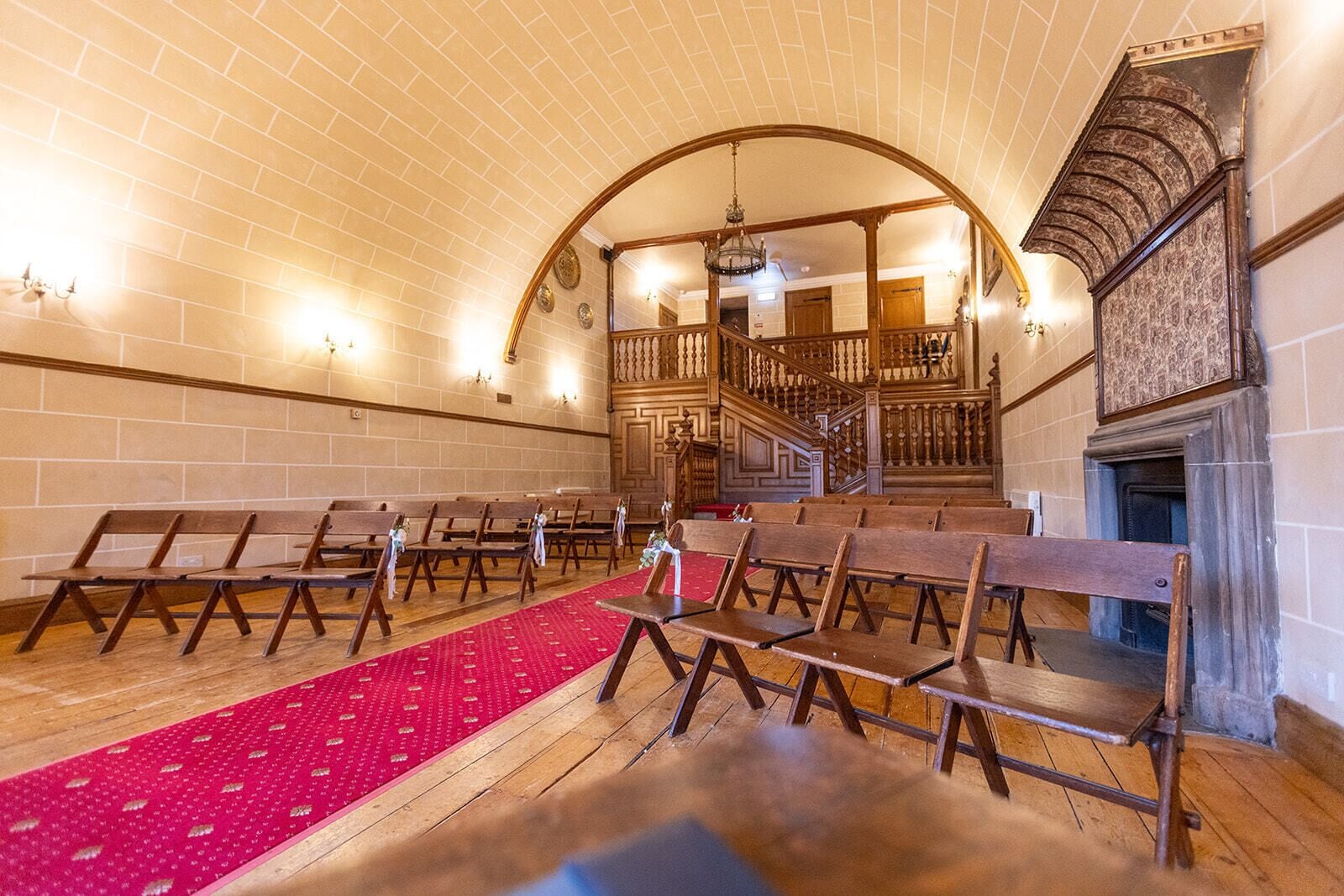 Interior de iglesia con bancas de madera, alfombra roja, escalera de madera y chimenea.