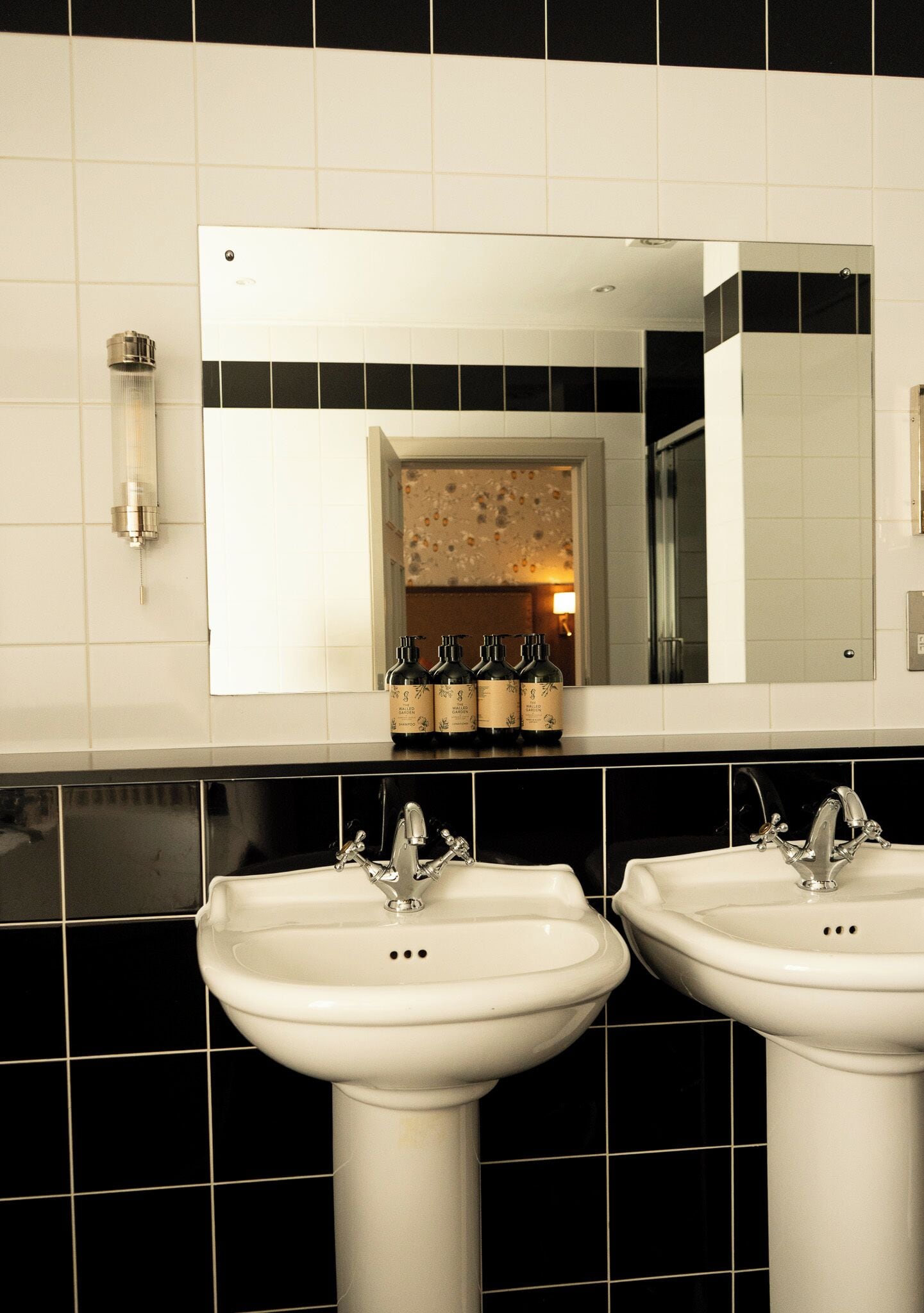 Un baño con dos lavamanos, un espejo y un aplique de pared.