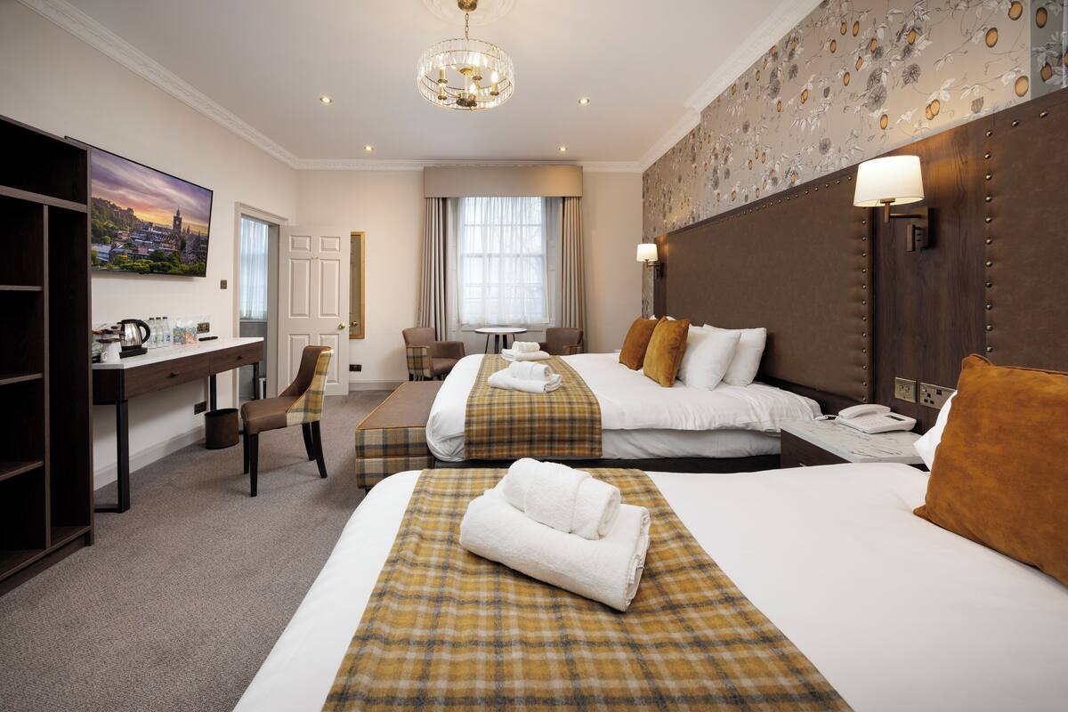 A hotel room with two beds, a desk, a chair, a table, and a large window.