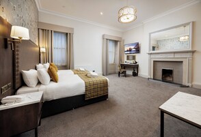 A hotel room with a large bed, a desk, a fireplace, and a television.