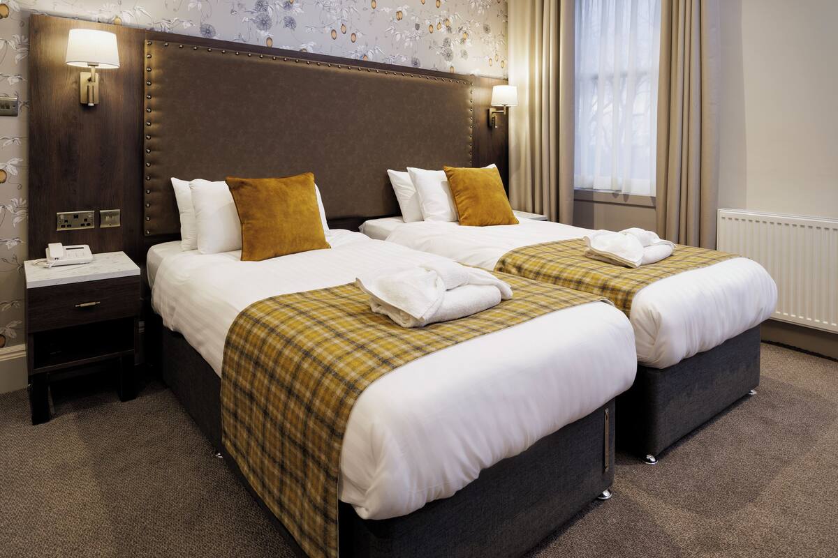 A hotel room with two beds, a nightstand with a phone, and a window with curtains.