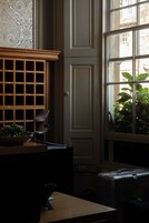 A room with a large window, a wooden cabinet with drawers, a table with a chair, and a bench.