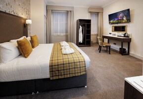 Habitación de hotel con cama, escritorio, silla, armario y televisor en la pared.