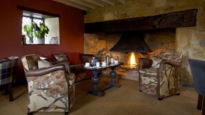 A cozy living room with a fireplace, comfortable seating, and a window with plants. - The Broadway Hotel (Broadway)