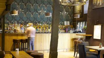 Un área de bar con mostrador de madera, taburetes y un cantinero.
