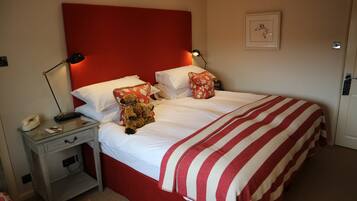 A neatly made bed with a red headboard, white bedding, and a striped blanket. There is a bedside table with a lamp, a teddy bear, and a telephone.