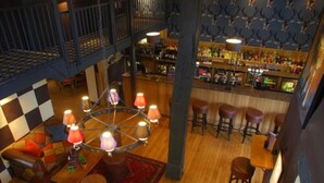 A bar area with a high ceiling, a circular chandelier, and a checkered wall pattern. - The Broadway Hotel (Broadway)