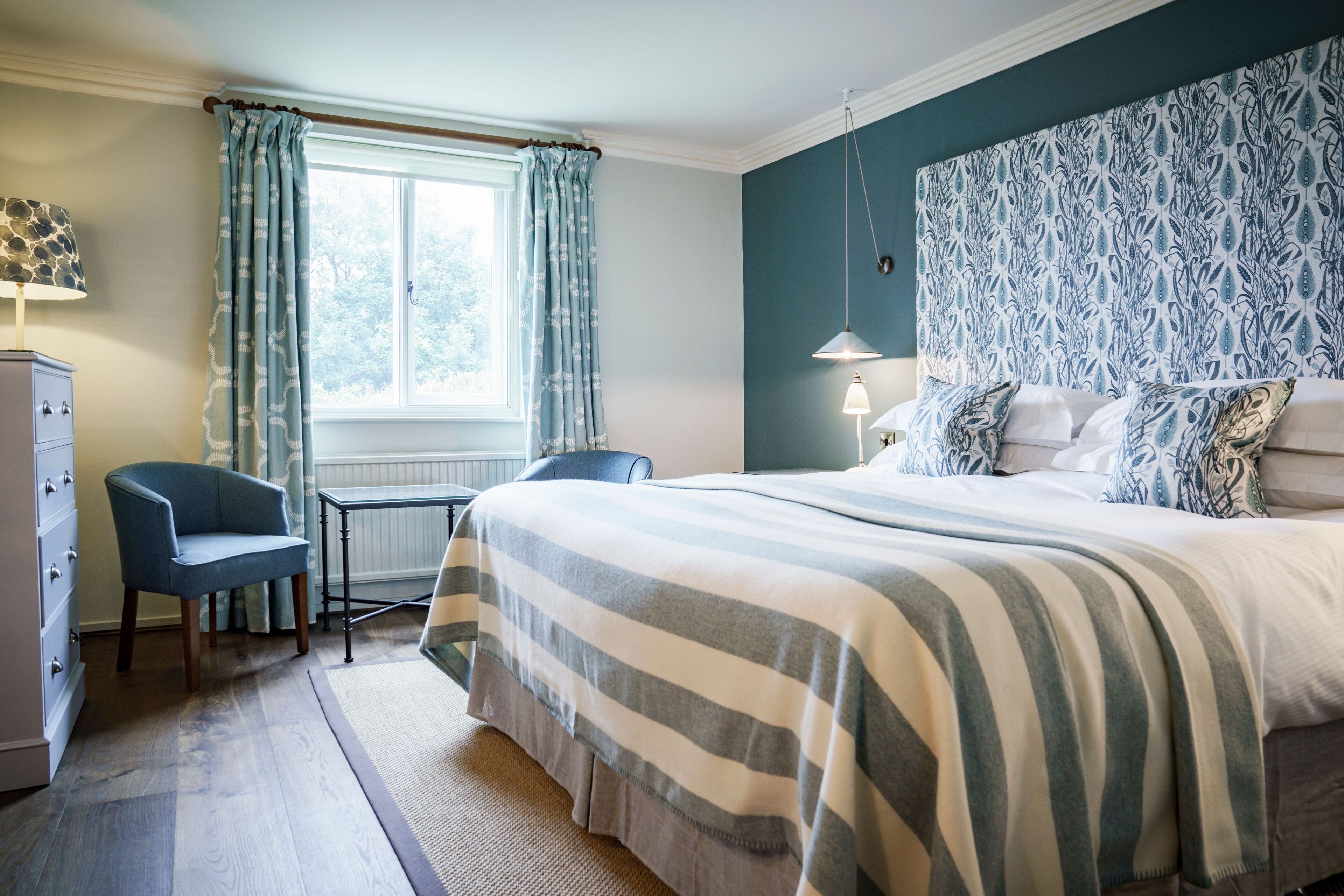 A bedroom with a bed, a chair, a desk, and a window with curtains.
