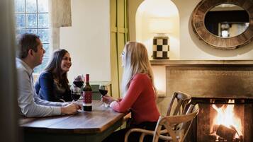 A dining area with a fireplace, wooden chairs, and a table with wine bottles and glasses.
