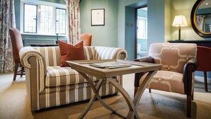 A living room with a striped sofa, a red armchair, a wooden coffee table, and a lamp. - Bear of Rodborough Hotel (Stroud)