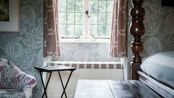 A room with a bed, a small table, a window with curtains, and patterned wallpaper.