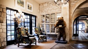A room with stone walls, large windows, and a bear statue. There are two patterned chairs and a chandelier. - Bear of Rodborough Hotel (Stroud)