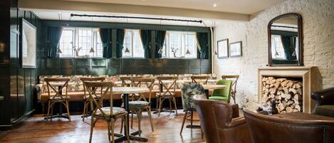A cozy restaurant with wooden furniture, a stone wall, and a large window with curtains.