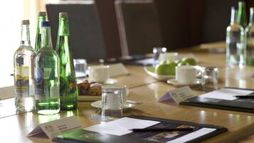 A conference table with green glass bottles, a glass of water, a cup, and a plate with croissants.