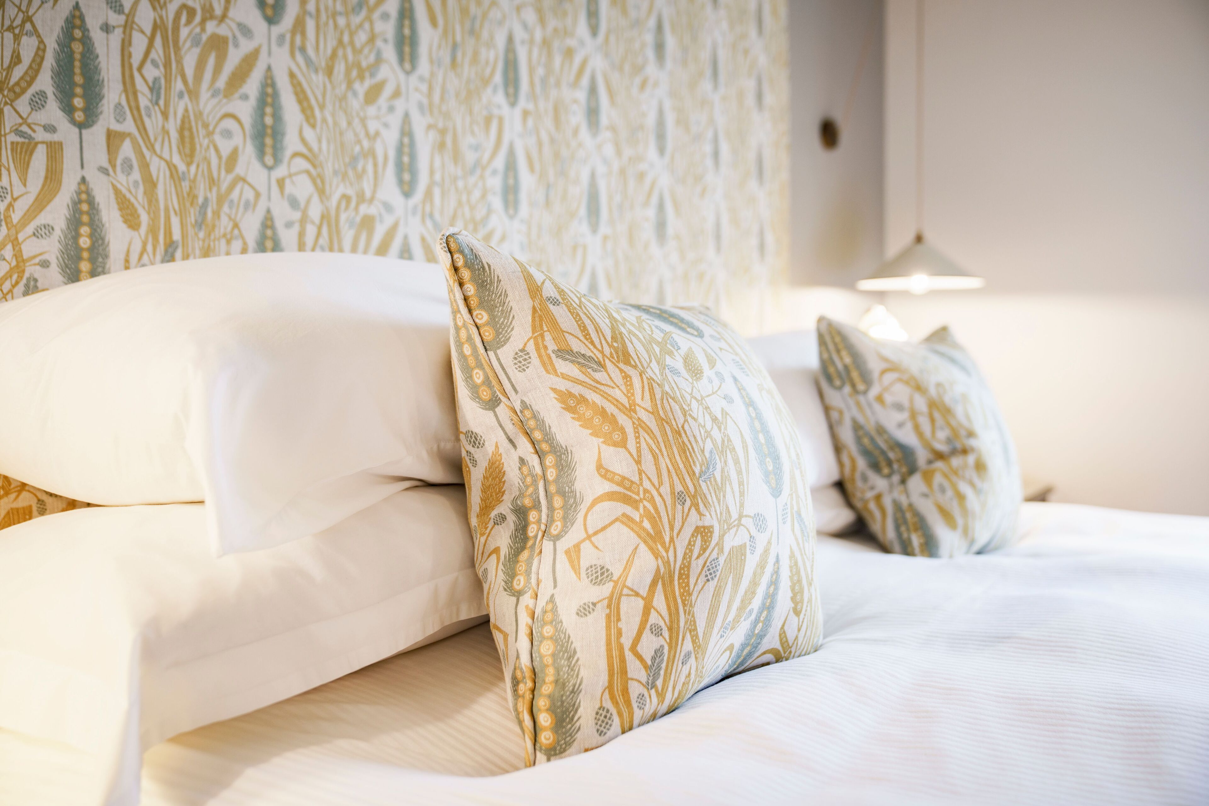 Una cama bien hecha con sábanas blancas y almohadones decorativos con motivos naturales.