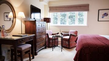 Een slaapkamer met een bed, een dressoir, een bureau met stoel, een tafel, een spiegel en een raam met jaloezieën.