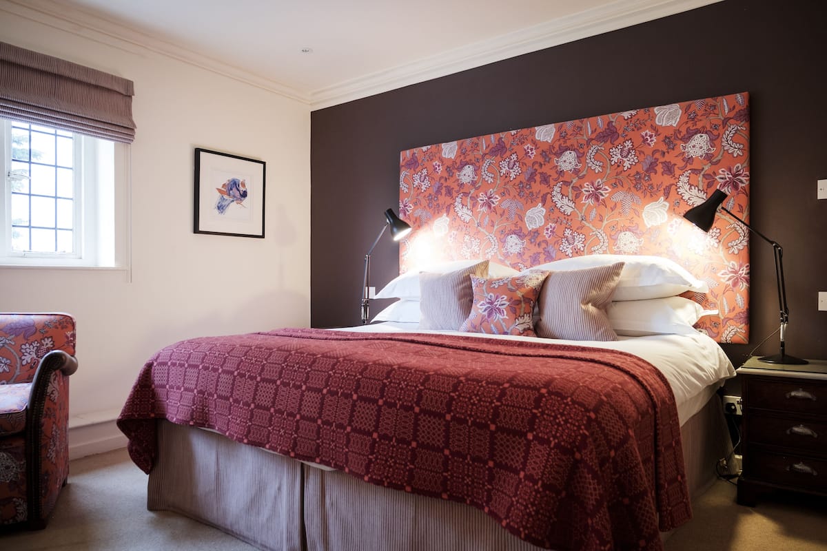 A bedroom with a large bed, a nightstand, a chair, a window with curtains, and a framed picture on the wall.