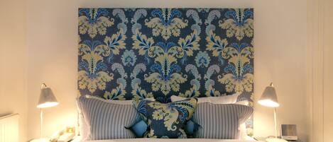 Una cama bien hecha con almohadas a rayas, un cabecero estampado y lámparas de noche.