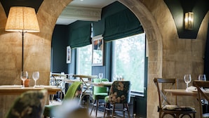 A restaurant with stone arches, wooden tables, and chairs. - Bear of Rodborough Hotel (Stroud)