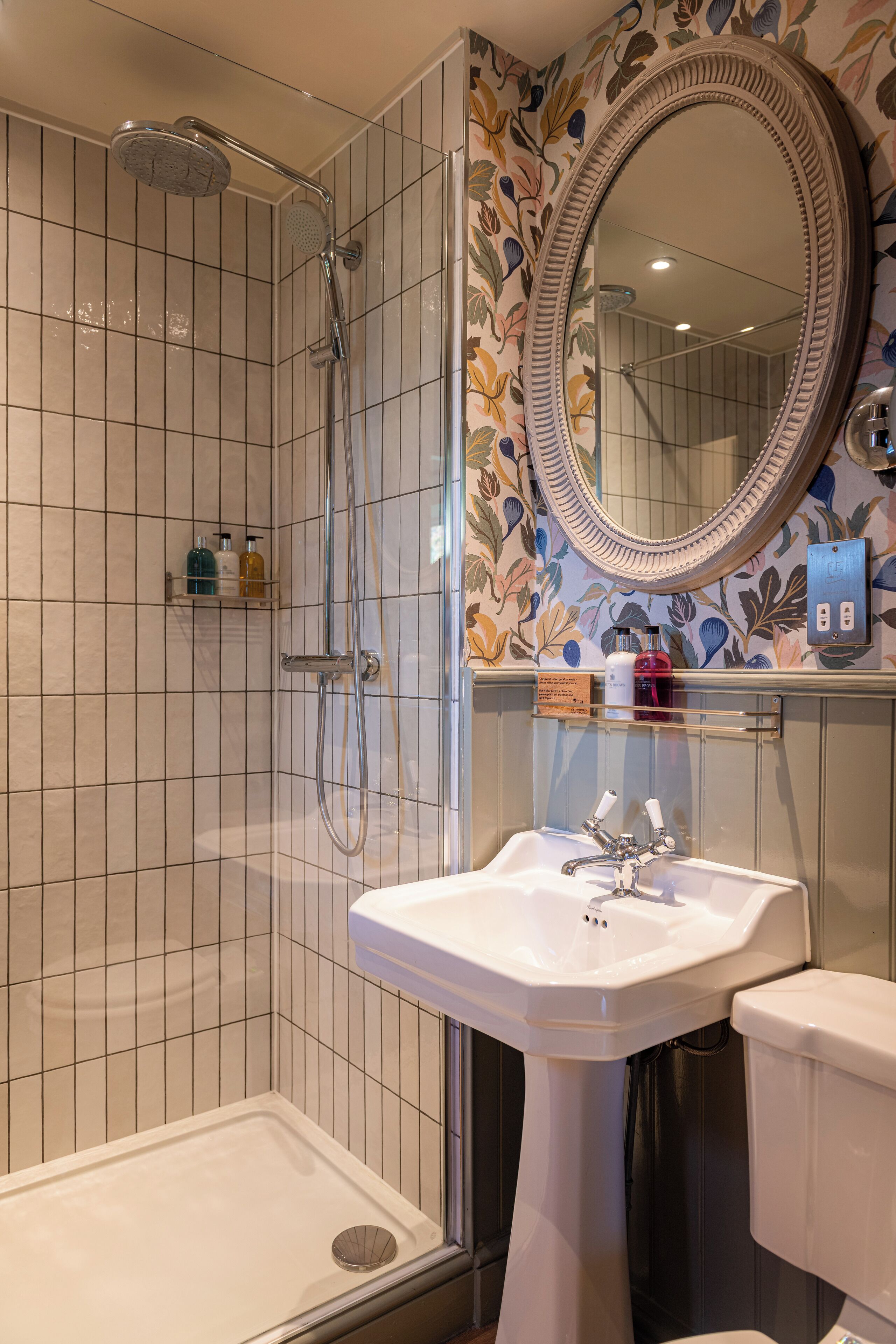 A bathroom with a shower, a sink, a toilet, and a decorative mirror.