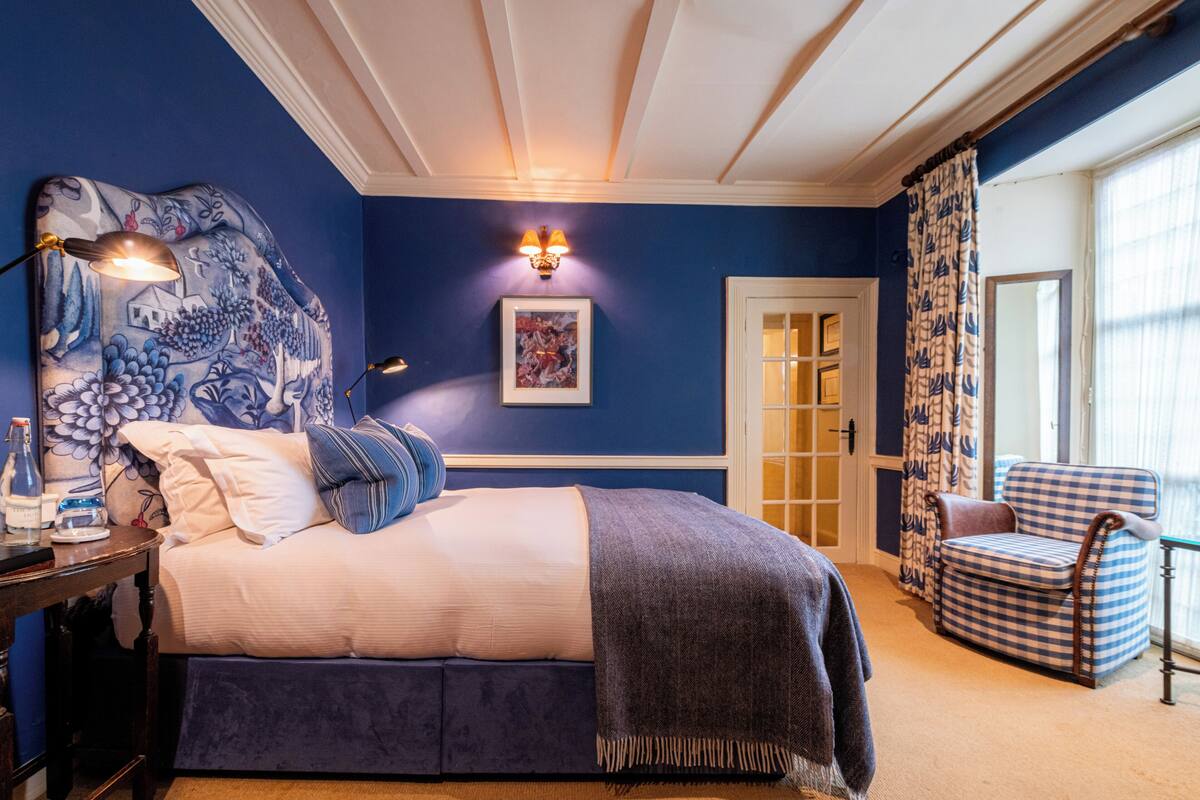 Quarto com cama, cadeira, abajur, quadro na parede e porta.