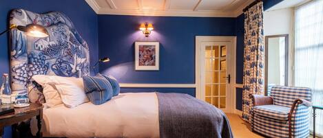 A bedroom with a bed, a chair, a lamp, a picture on the wall, and a door.