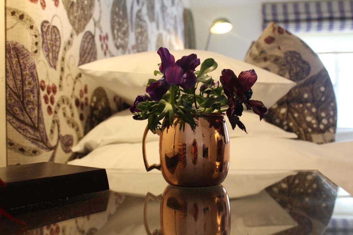Uma cama com almofadas estampadas, um vaso com flores e um abajur em um quarto de hotel.