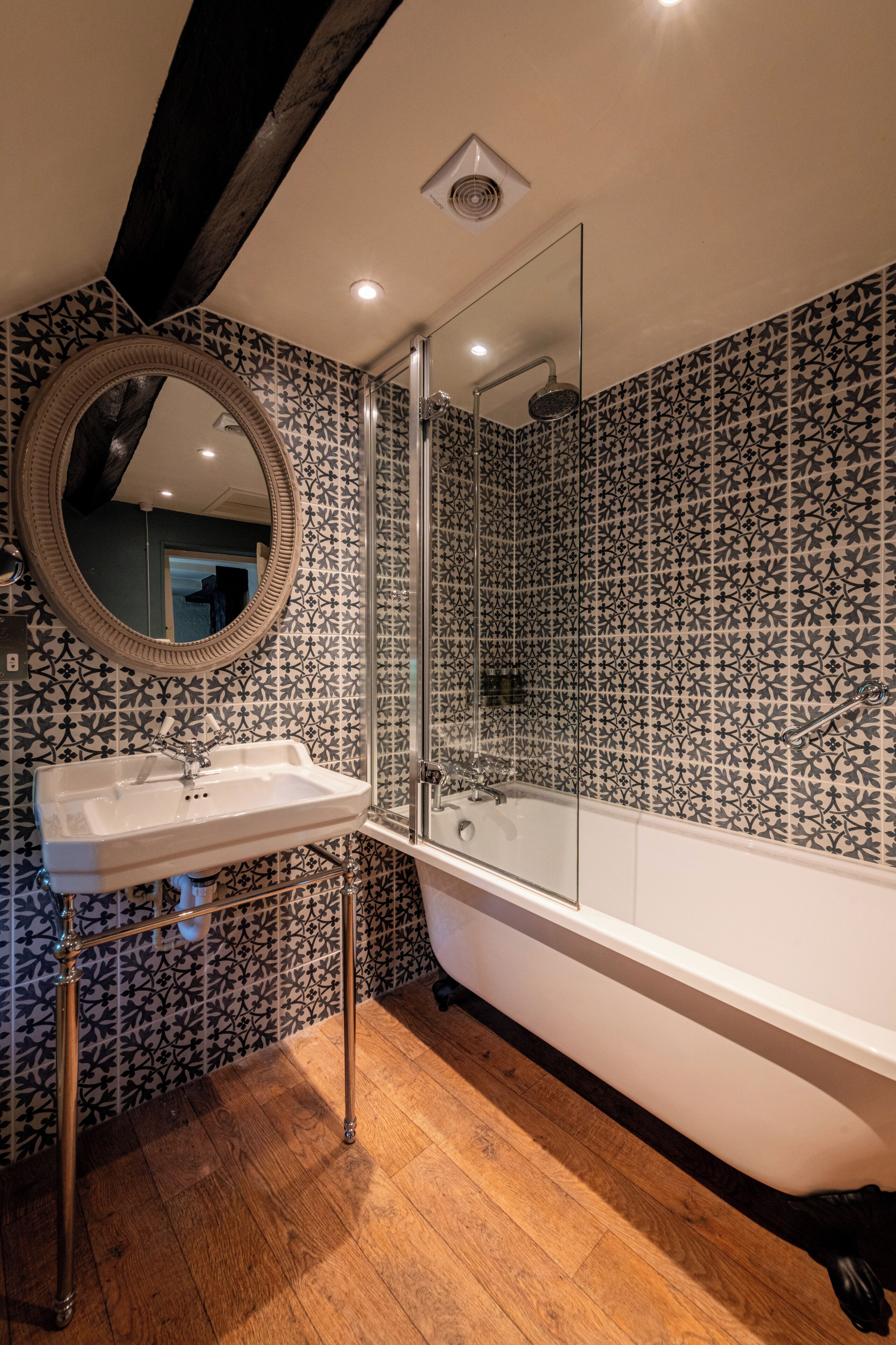 A bathroom with a freestanding bathtub, a sink with a mirror, and patterned tile walls.