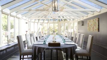 A long table set for a meal in a room with a high ceiling and large windows.