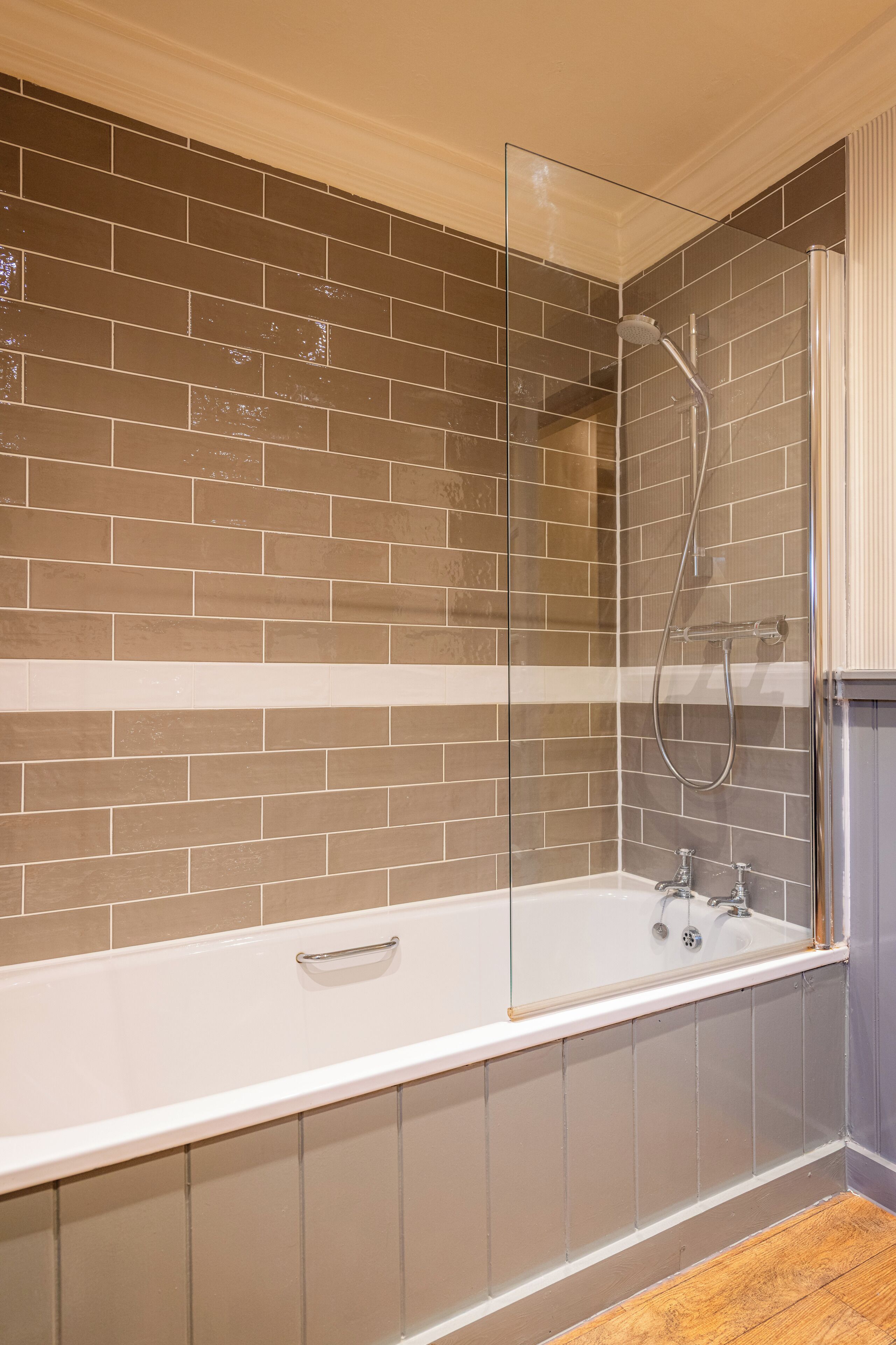 A bathroom with a glass-enclosed shower, a white bathtub, and brown tiled walls.