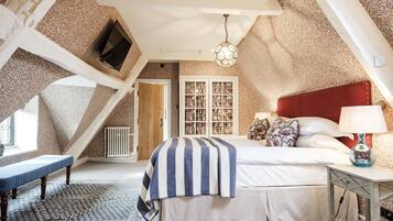 A bedroom with a sloped ceiling, a bed with a striped blanket, a bedside table with a lamp, and a patterned rug.
