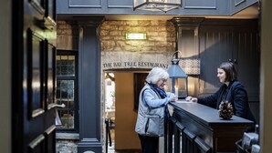 A woman at a counter in a restaurant with a sign above reading "The Bay Tree Restaurant." - Bay Tree Hotel (Burford)